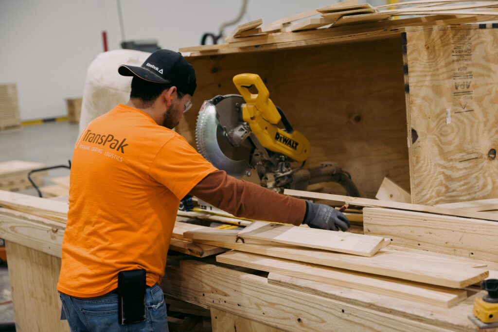 Worker in a TransPak warehouse using a circular saw to cut pieces of wood.