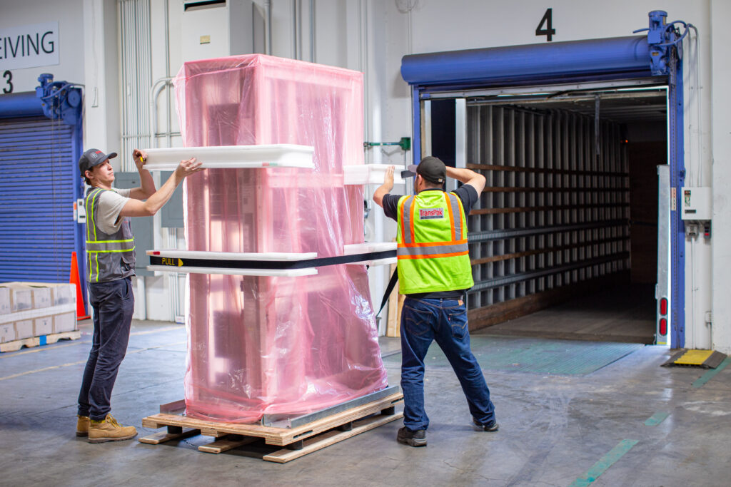 TransPak team members securing and preparing a server rack shipment with protective packaging and load stabilization at a loading dock facility.