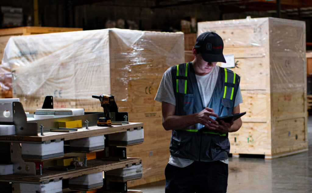 TransPak employee inspecting reusable server rack transport pallets and engineered packaging components inside a warehouse facility.