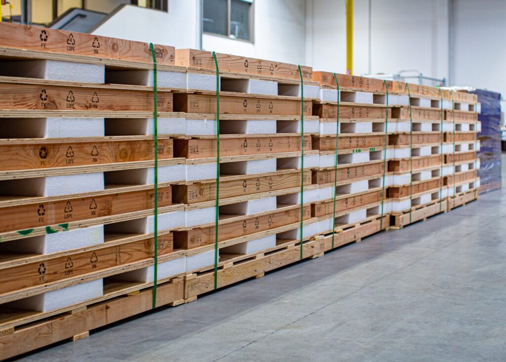 Stacks of wooden pallets with white foam insulation boards in a warehouse.