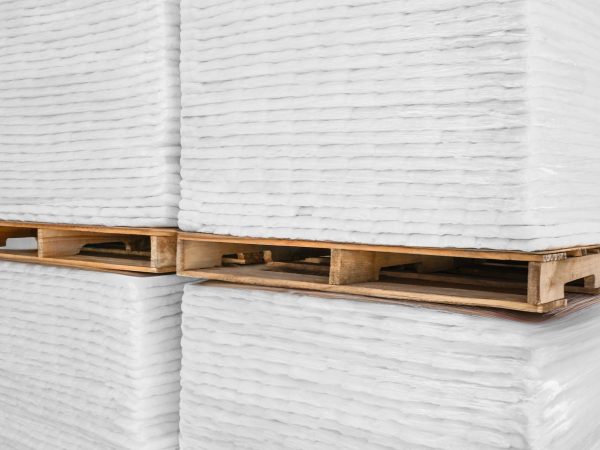 Stacks of white foam sheets on wooden pallets in a warehouse setting.